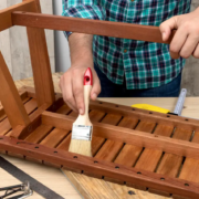 Carpenter applying varnish with a brush while assembling a wooden furniture piece.