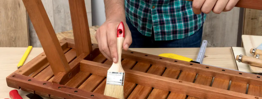 Carpenter applying varnish with a brush while assembling a wooden furniture piece.