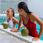 Two women relaxing in a swimming pool holding fresh coconuts by the poolside.